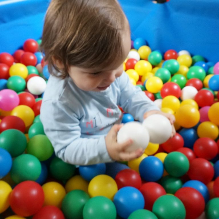 Ein Kleinkind sitzt vergnügt in einem bunten Bällebad.