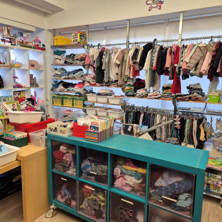 Blick in die Schatztruhe: Regale und Kleiderstangen mit gut sortierter Kinderkleidung, Kisten mit Büchern und Spielzeug.